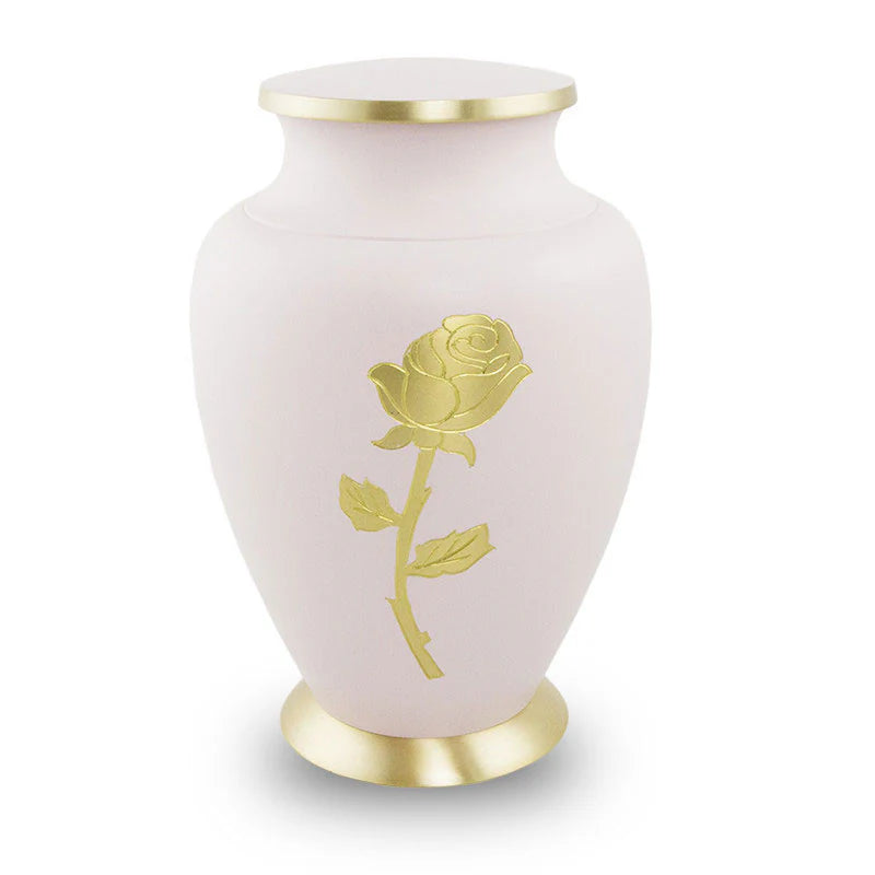 A bronze cremation urn with a light pink finish and a hand engraved rose on the front. The urn has a gold-colored lid and base.