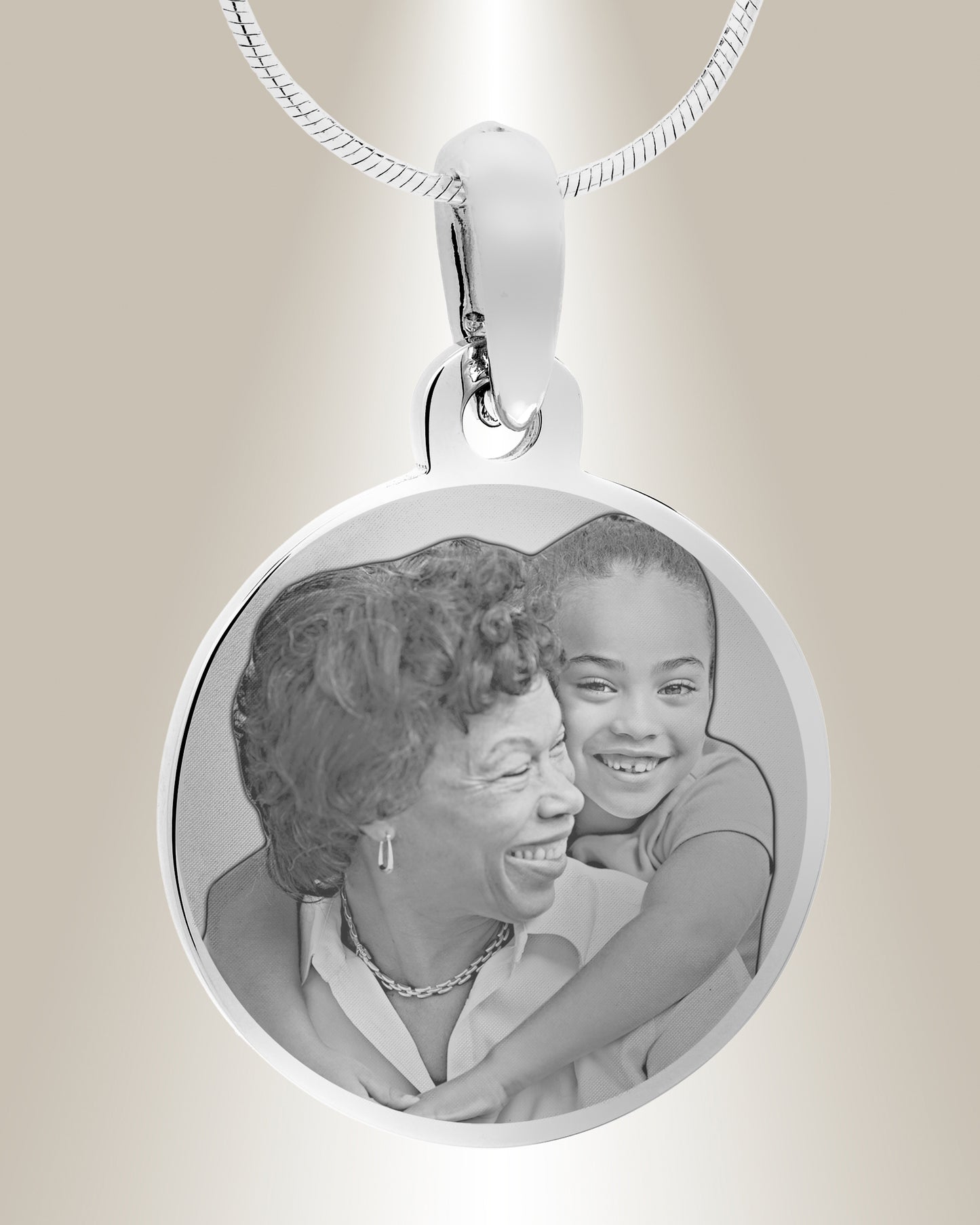 A stainless steel circle photo pendant with an engraved image of a smiling pair. The pendant is attached to a silver chain.