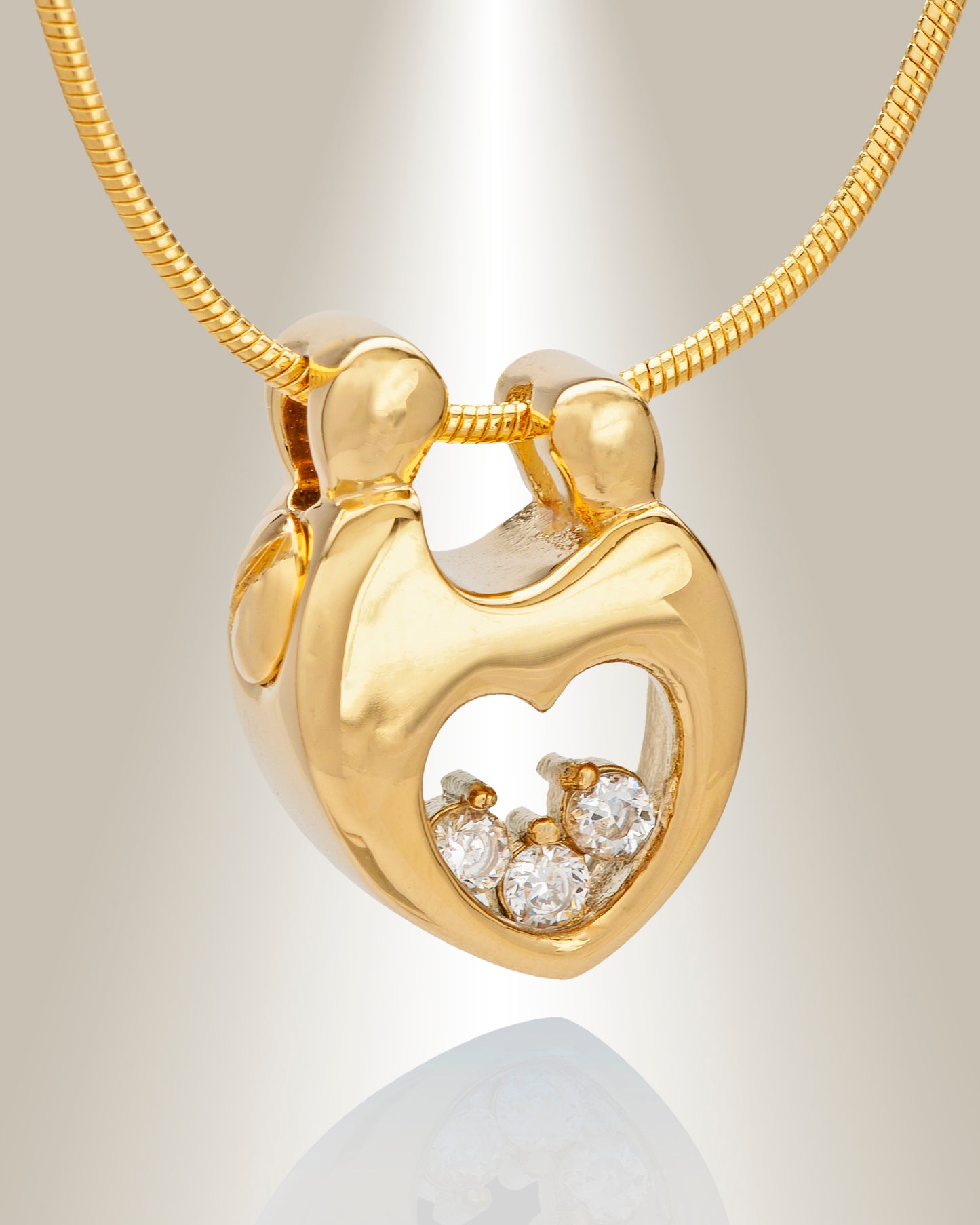 A gold-colored heart-shaped pendant with the silhouette of two people at the center and three gemstones at the bottom, displayed on a chain.