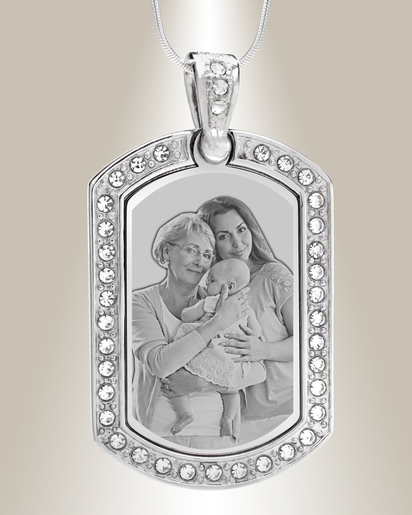 A stainless steel dog tag pendant with a photo engraving of two individuals and surrounded by clear gemstones. The pendant is attached to a silver chain.