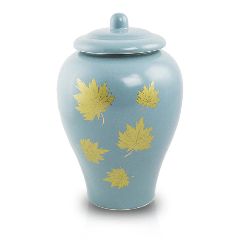 A blue ceramic urn with golden hand painted leaves on it, with a lid on top.