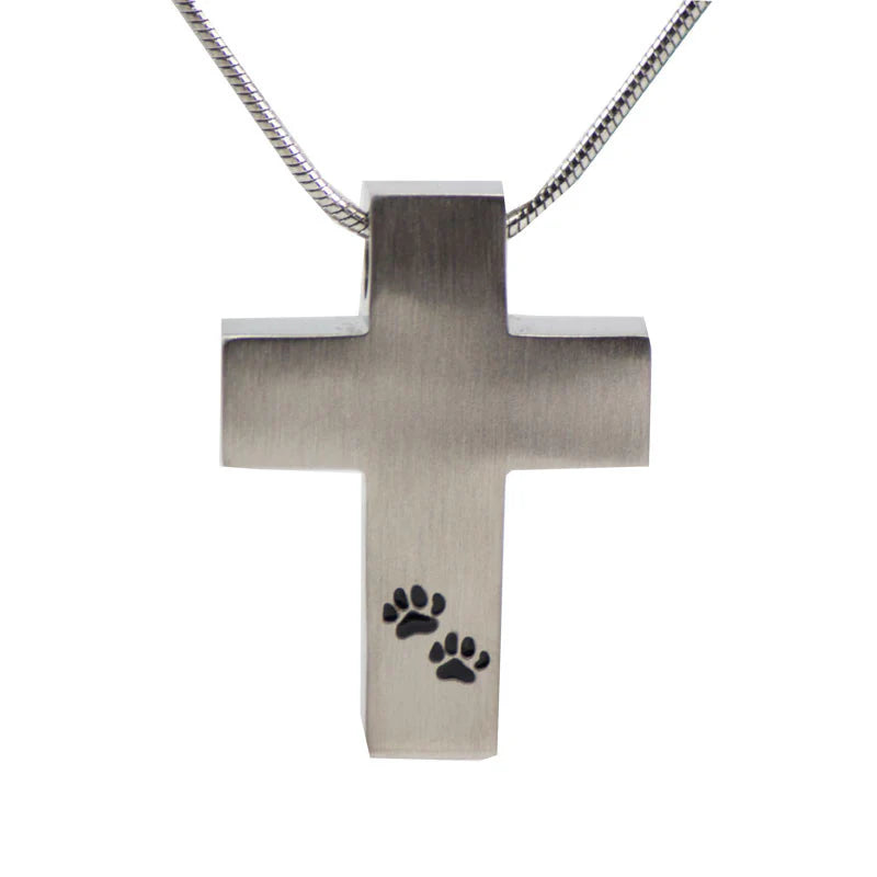 A stainless steel cross cremation pendant with two small paw prints engraved on the front, accompanied by an 18-inch pewter color snake chain.