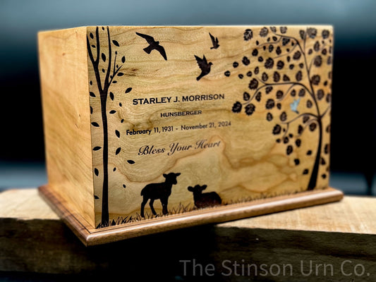 A wooden urn with engravings of trees, leaves, a dove, sheep, and birds on it, standing on a wooden surface.