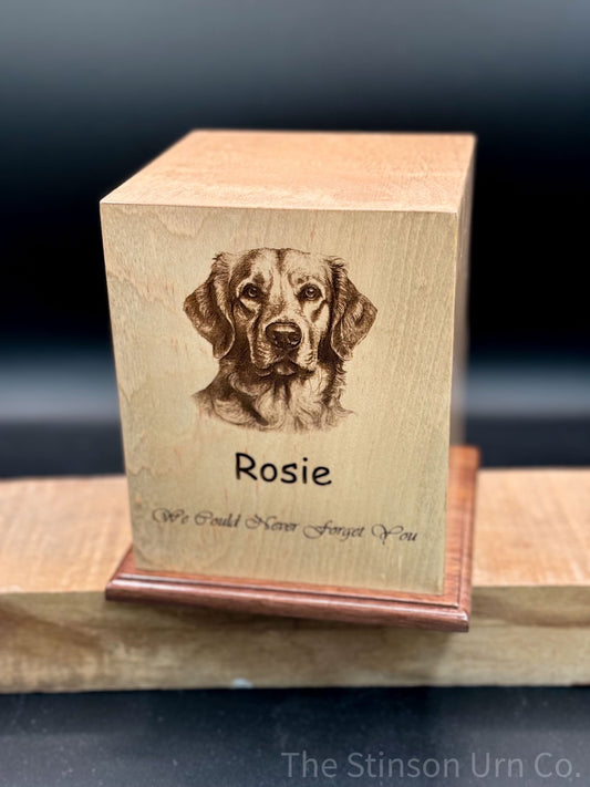 A wooden pet photo urn with a cherry base, featuring an engraved image of a dog's head on the front, along with a name and a phrase.