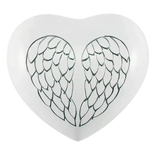 A heart-shaped, white-finished brass cremation urn with hand engraved angel wings on the front.