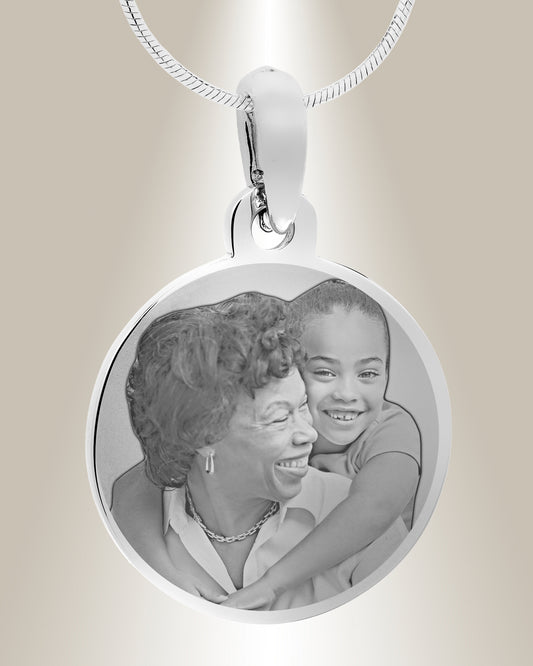 A stainless steel circle photo pendant with an engraved image of a smiling pair. The pendant is attached to a silver chain.