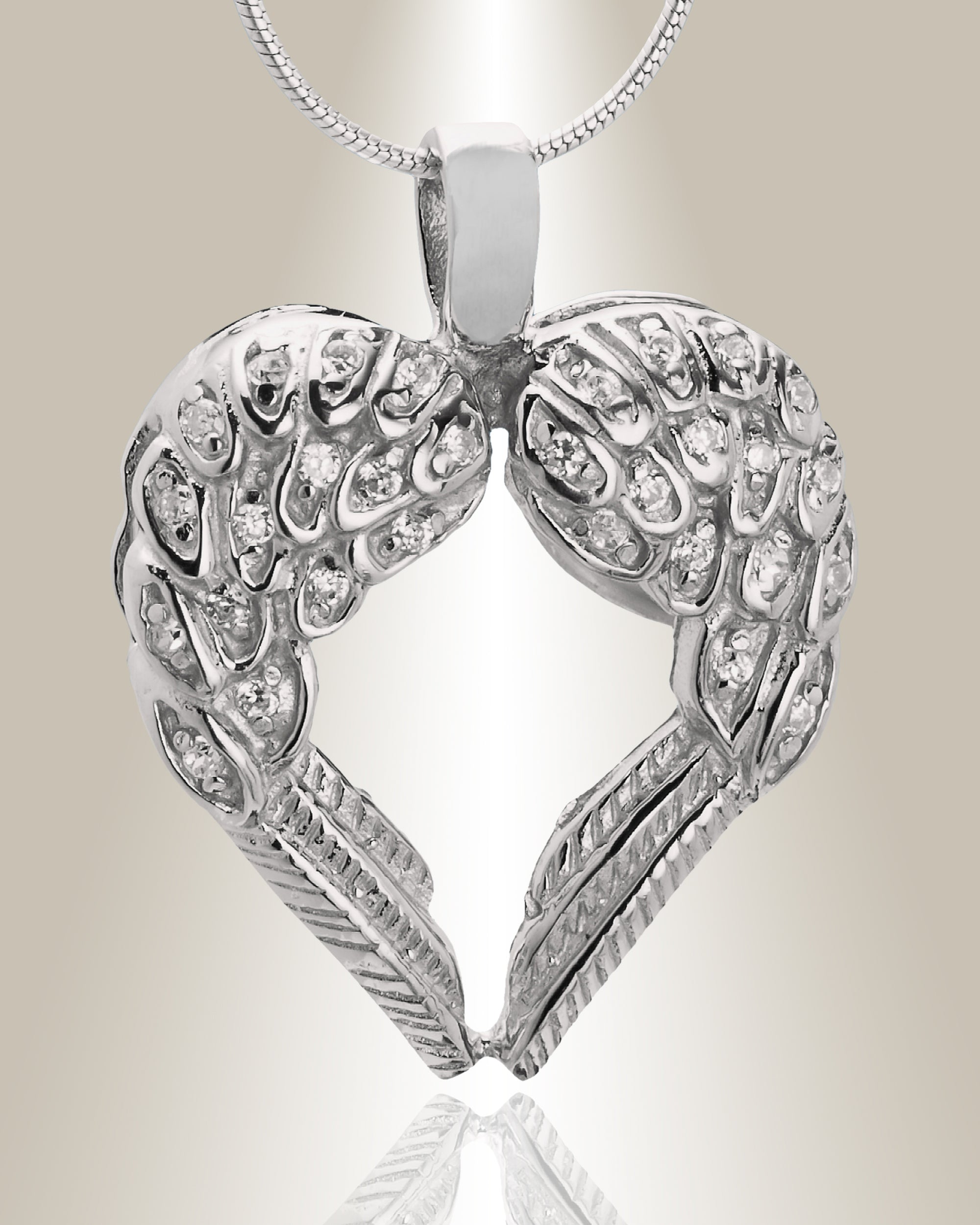 A silver cremation pendant in the shape of a heart with two wings, featuring gemstone accents at the top. The pendant is designed to hold ashes and comes with a chain.