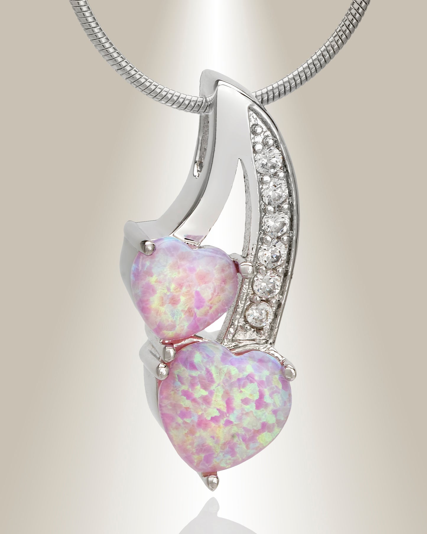 A silver cremation pendant featuring two heart-shaped pink opals with accent clear gemstones on the stem, designed to hold ashes inside.