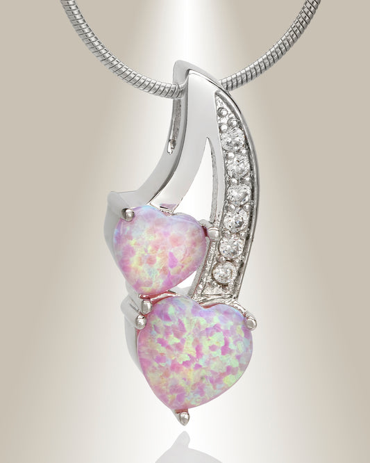 A silver cremation pendant featuring two heart-shaped pink opals with accent clear gemstones on the stem, designed to hold ashes inside.