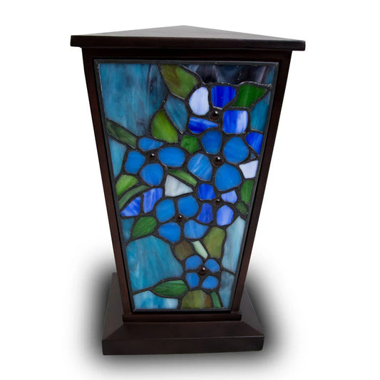 A hand made cremation urn with blue and natural color forget-me-not flowers on the panel design, set within a resin frame.