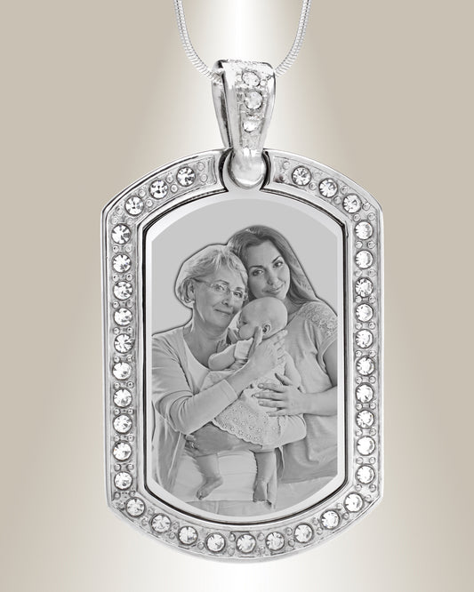 A stainless steel dog tag pendant with a photo engraving of two individuals and surrounded by clear gemstones. The pendant is attached to a silver chain.