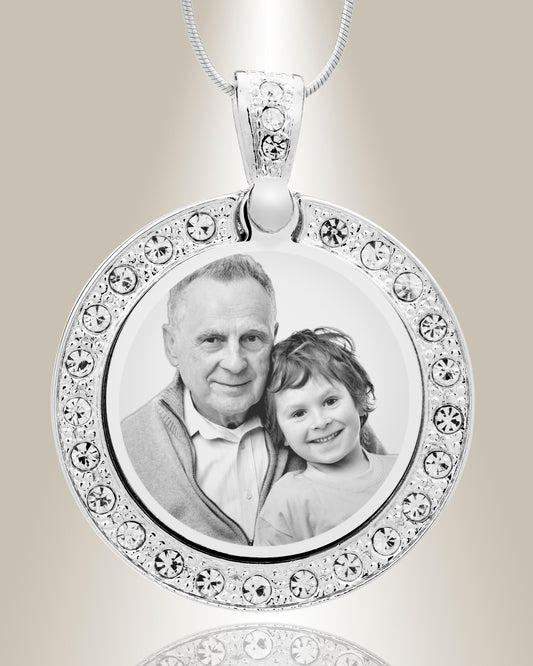 A stainless steel circle photo pendant with clear gemstones around the border, displaying an engraved photo of an older man and a young child.