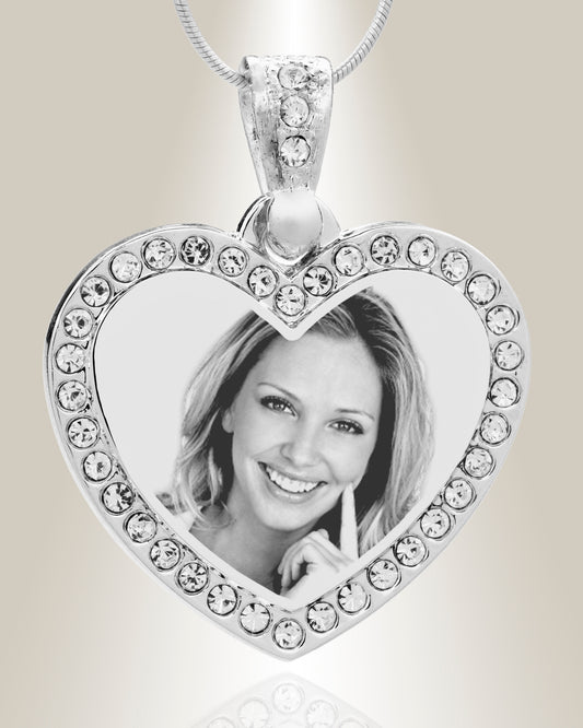 A heart-shaped stainless steel pendant with a photo engraved in the center, surrounded by clear gemstone accents, attached to a silver chain.