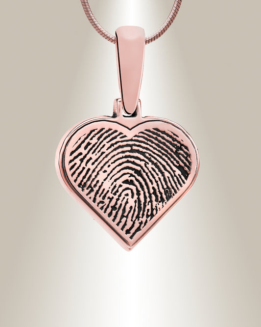 A heart-shaped silver pendant with a fingerprint engraving on the front. The pendant appears to be attached to a chain.