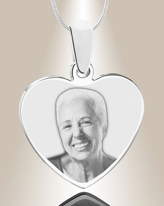 A stainless steel heart-shaped pendant with an engraved photo of a smiling person inside. The pendant is accompanied by a 20-inch chain.