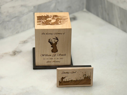 A wooden urn with an engraving of a dog retrieving a fish on top and a buck on the front, alongside a smaller companion urn with a different design.