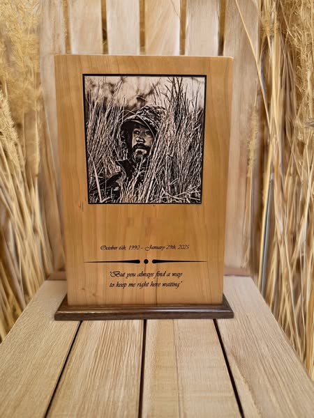 A wooden photo urn with an engraved black and white photo of a person. The urn is placed on a wooden surface with a wooden backdrop.