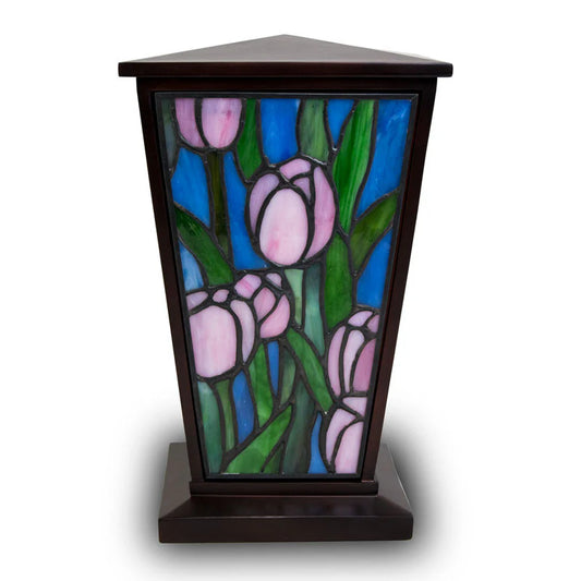 A stained glass cremation urn with a pink tulip design on one side, supported within a resin frame.