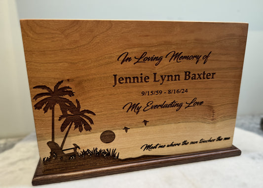 A wooden urn with an engraved beach scene and text honoring an individual.