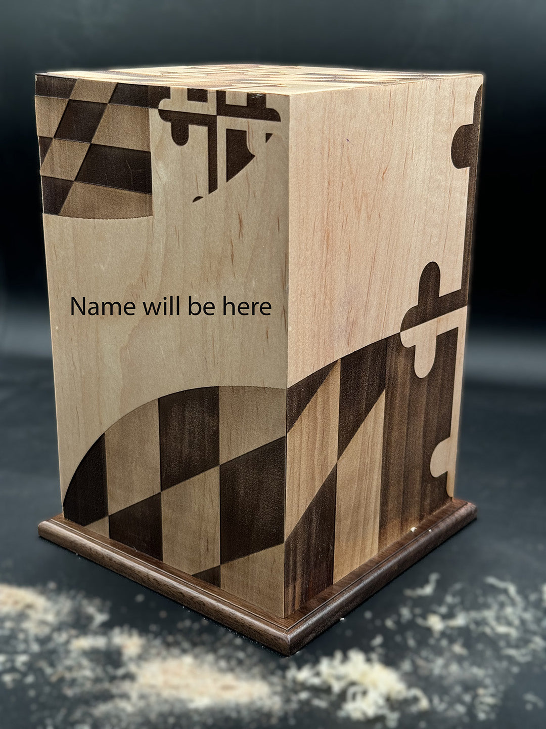 A wooden urn with a Maryland State Flag, featuring a placeholder for a name, on a wooden surface.