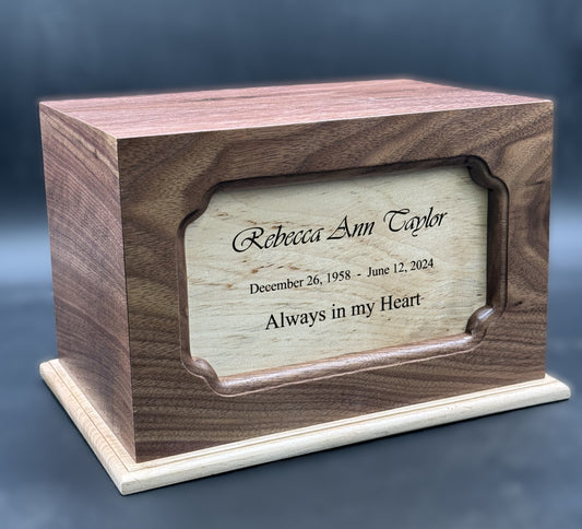 A wooden urn with a plaque on the front displaying personalized text. The urn has a combination of walnut and maple woods, with a visible grain pattern.