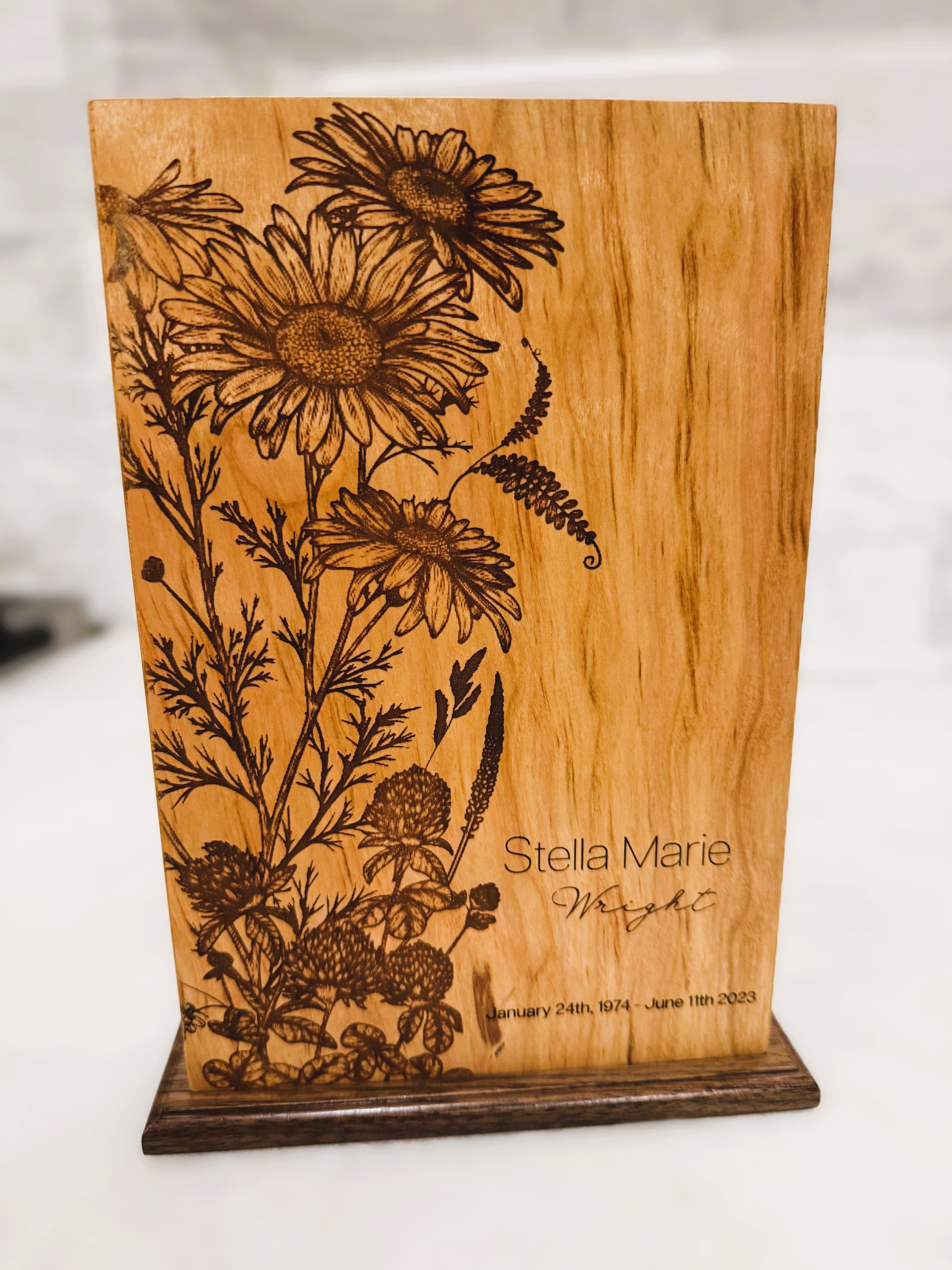 A wooden urn with floral engravings, featuring a walnut base, and personalized engraving on the front.