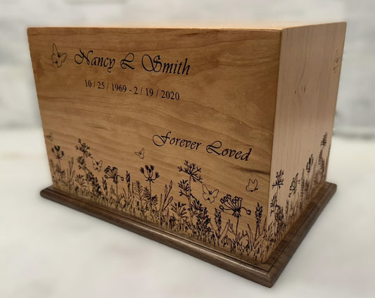 An engraved wooden urn with a Cherry wood finish and a Walnut base, featuring floral patterns and personalized text.
