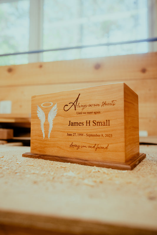 A wooden urn with a mother of pearl inlay in the shape of angel wings and halo, with engraved text on the side.