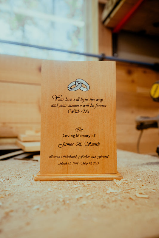 A wooden urn with engraved text, placed on a wooden surface, with a blurred background.