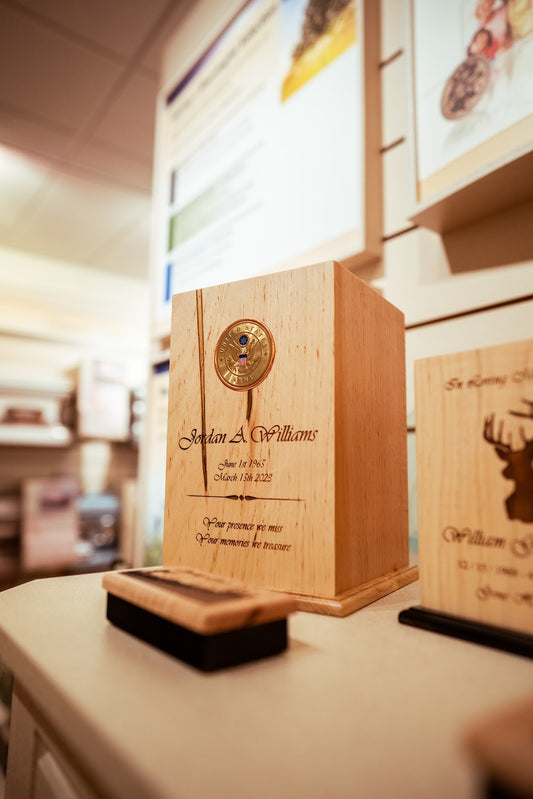 A wooden urn with a military emblem and engraved text, displayed on a table.