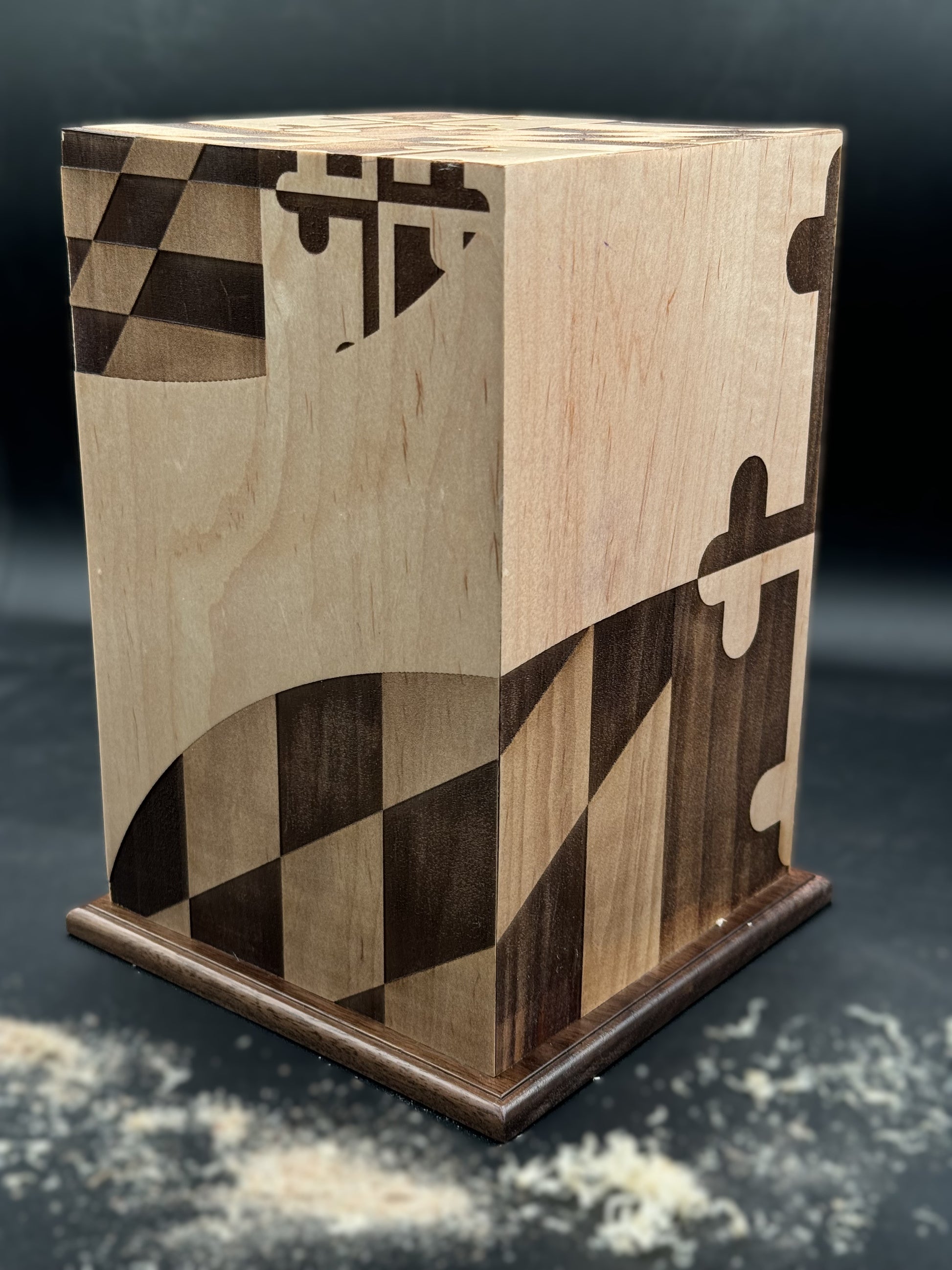 Handcrafted wooden urn with a Maryland state flag design, shown in a workshop setting with a chisel.