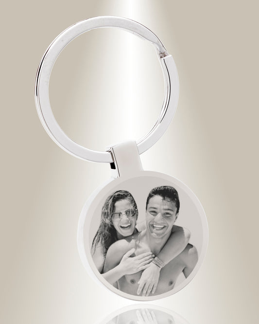 A round keychain with a photo engraved on it, featuring two individuals embracing.