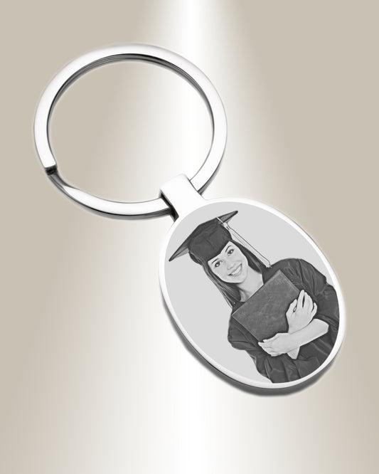 An oval-shaped keychain with a photo engraving of a person wearing a graduation cap and gown.