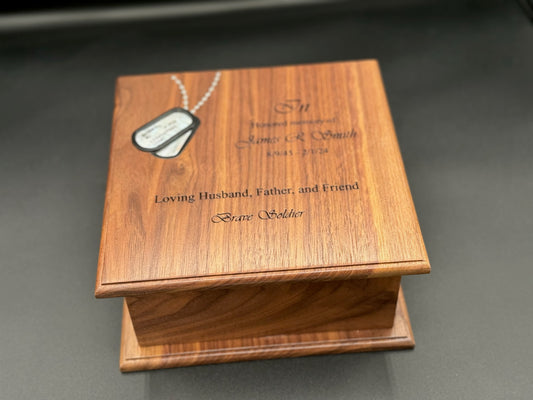 A wooden cremation urn with a set of military dog tags inlaid with white mother-of-pearl on the lid, alongside a personalized engraving on the front.